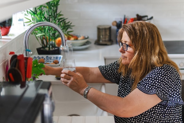 Woman filling a glass with clean water from a kitchen faucet